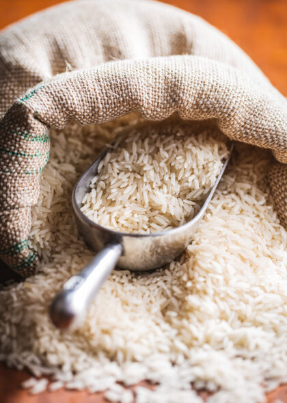 Uncooked white rice in burlap sack. Uncooked white rice in a burlap sack on wooden table.